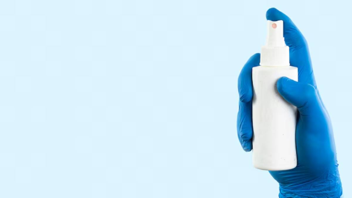 A gloved hand holds a white spray bottle against a light blue background, ready for use.