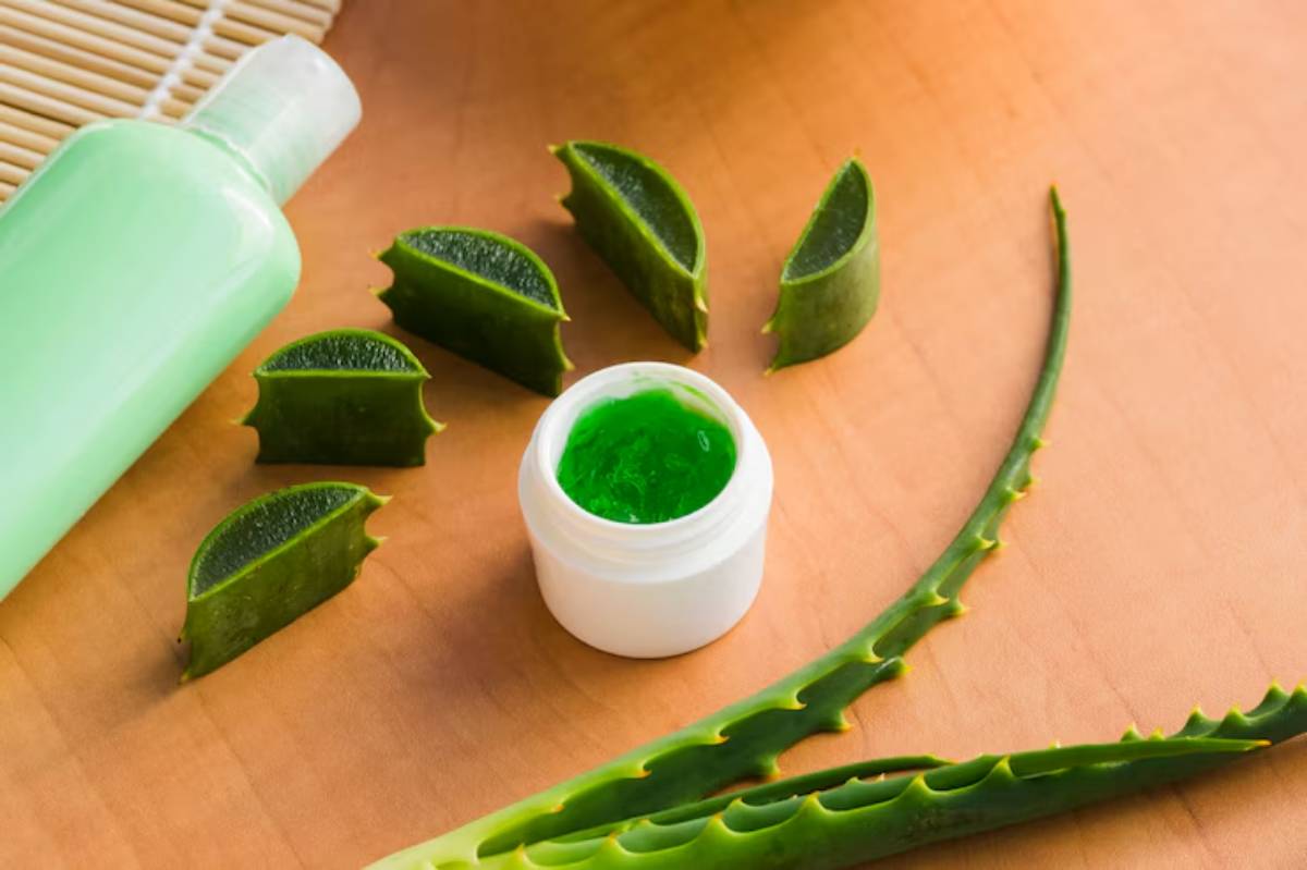 Aloe vera leaves, sliced pieces, a jar of green gel, and a green bottle on a wooden surface, showcasing natural skincare products. 