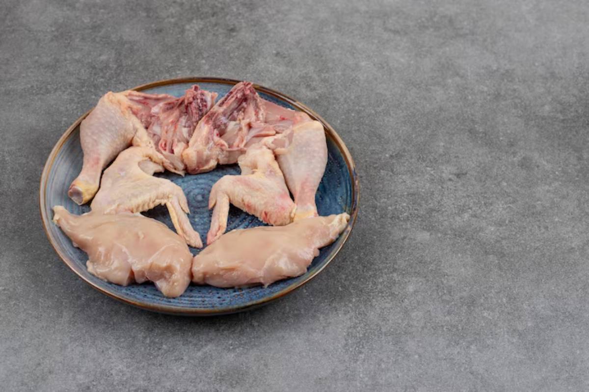  Raw chicken pieces arranged on a white plate against a gray background. 