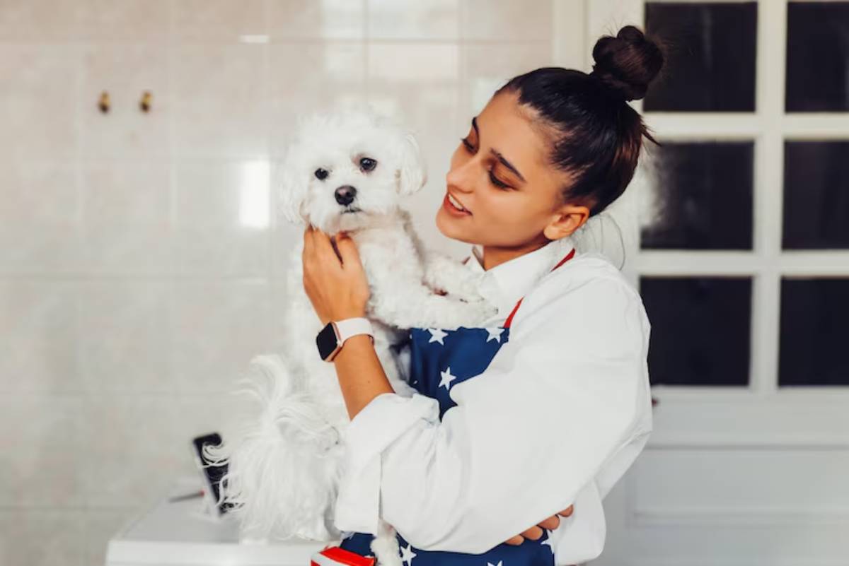 A woman in a star-patterned apron holds a small white dog, surrounded by a bright, modern kitchen.