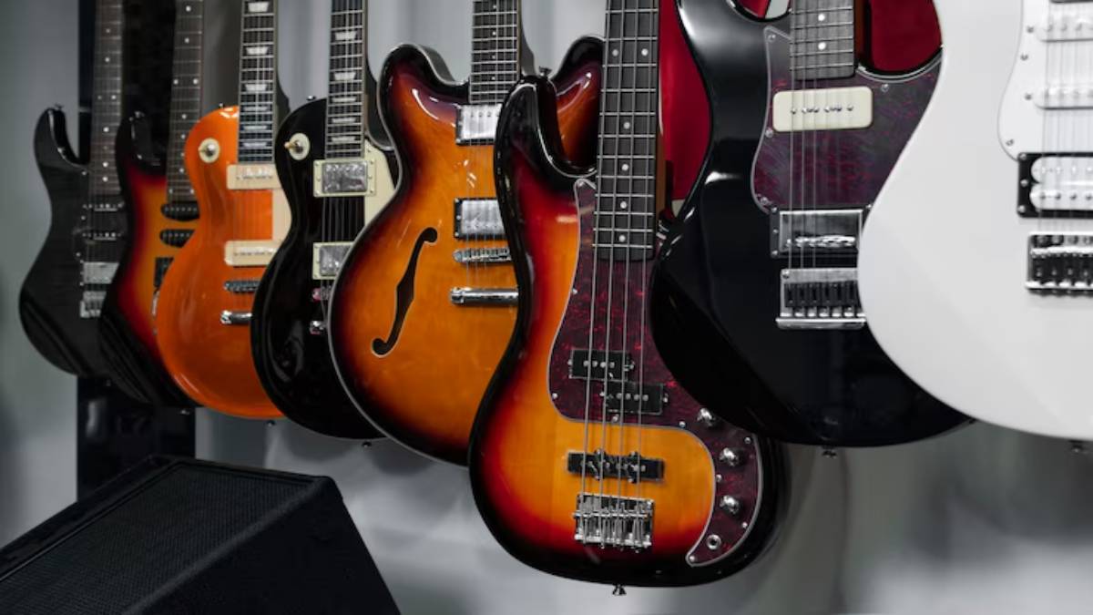  A collection of electric guitars and a bass guitar displayed on a wall, showcasing various shapes and finishes.